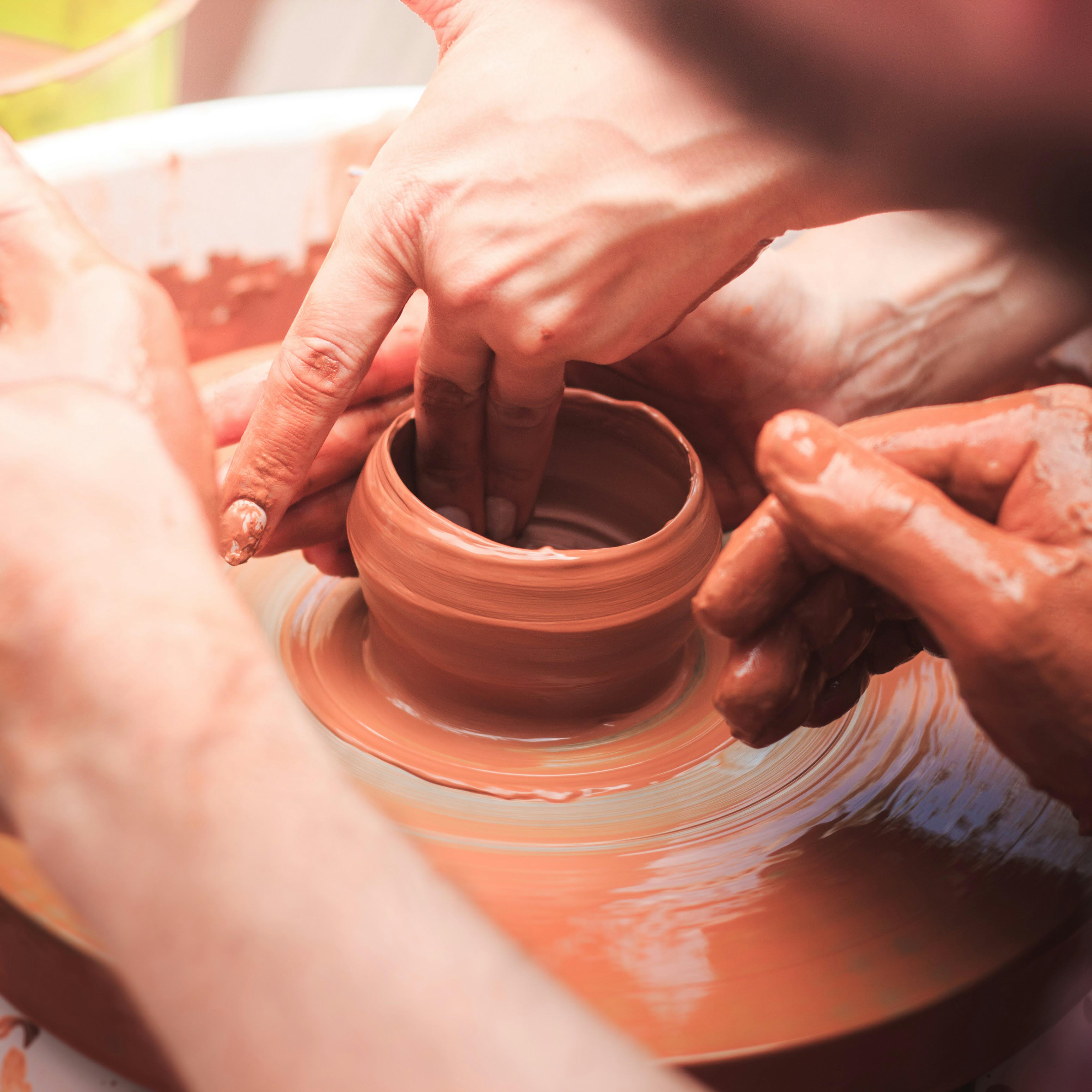 Tour de potier avec 4 mains en train de faire un vase en terre