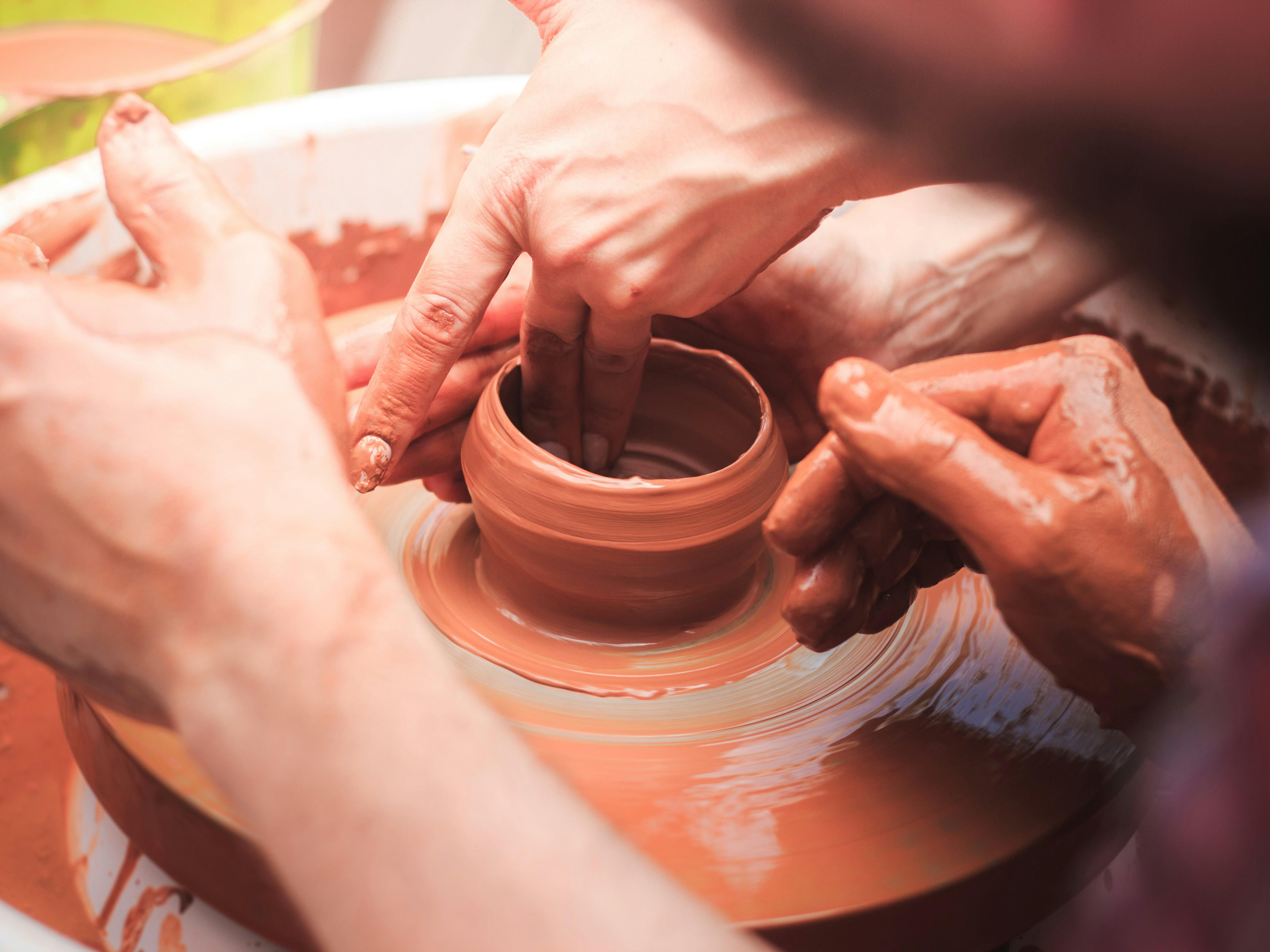 Tour de potier avec 4 mains en train de faire un vase en terre